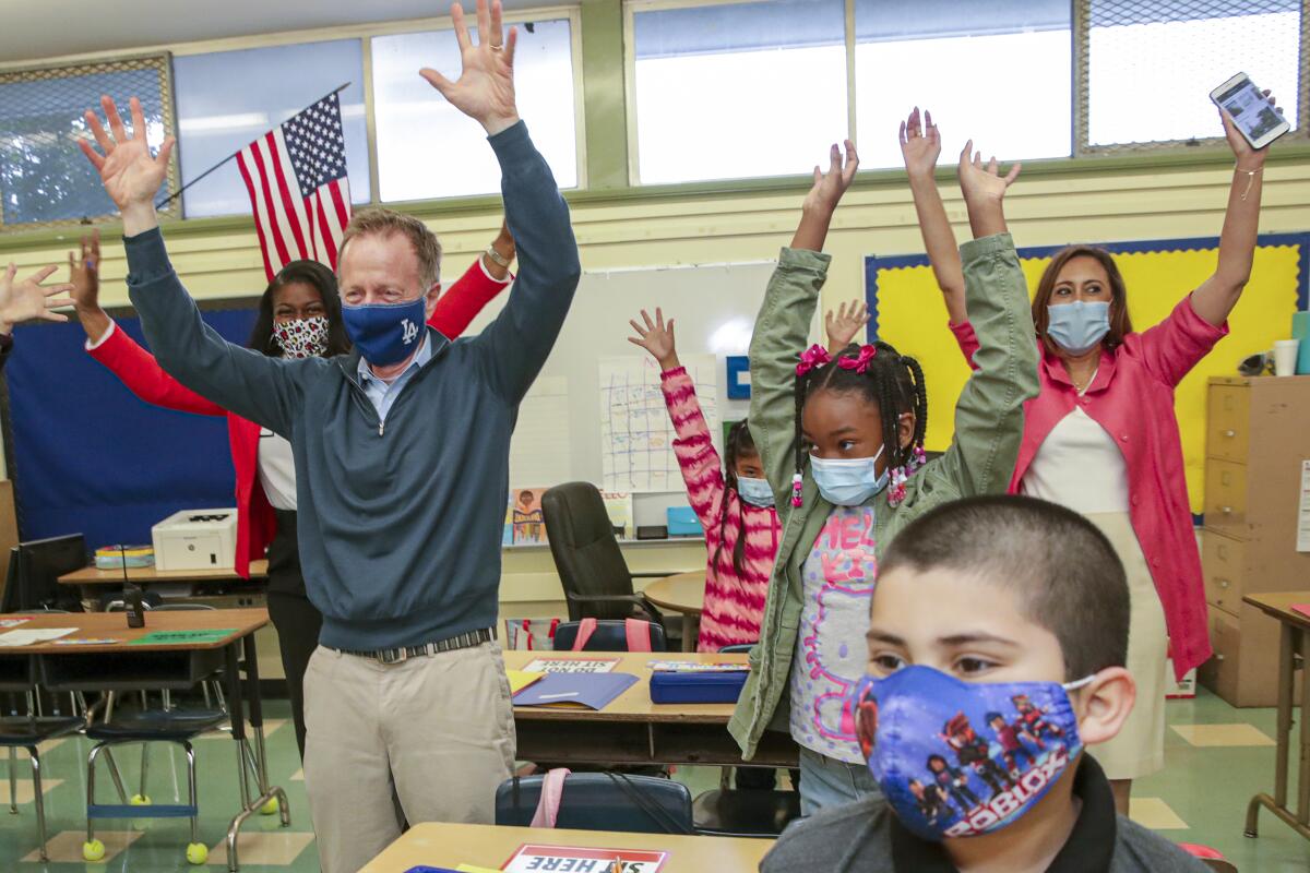 Children and school officials raise their arms. 