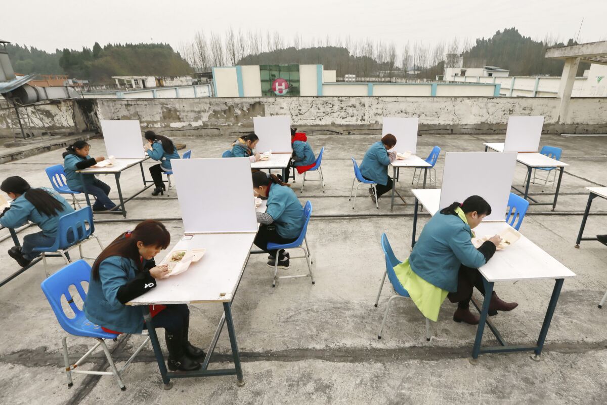 In this Friday, Feb. 14, 2020, photo, factory workers are separated by partitions as a precaution against infection as they take their lunch break on the roof of an electronics factory in Suining in southwestern China's Sichuan Province. China reported Saturday a figure of 2,641 new virus cases, a major drop from the higher numbers in recent days since a broader diagnostic method was implemented. (Chinatopix via AP)