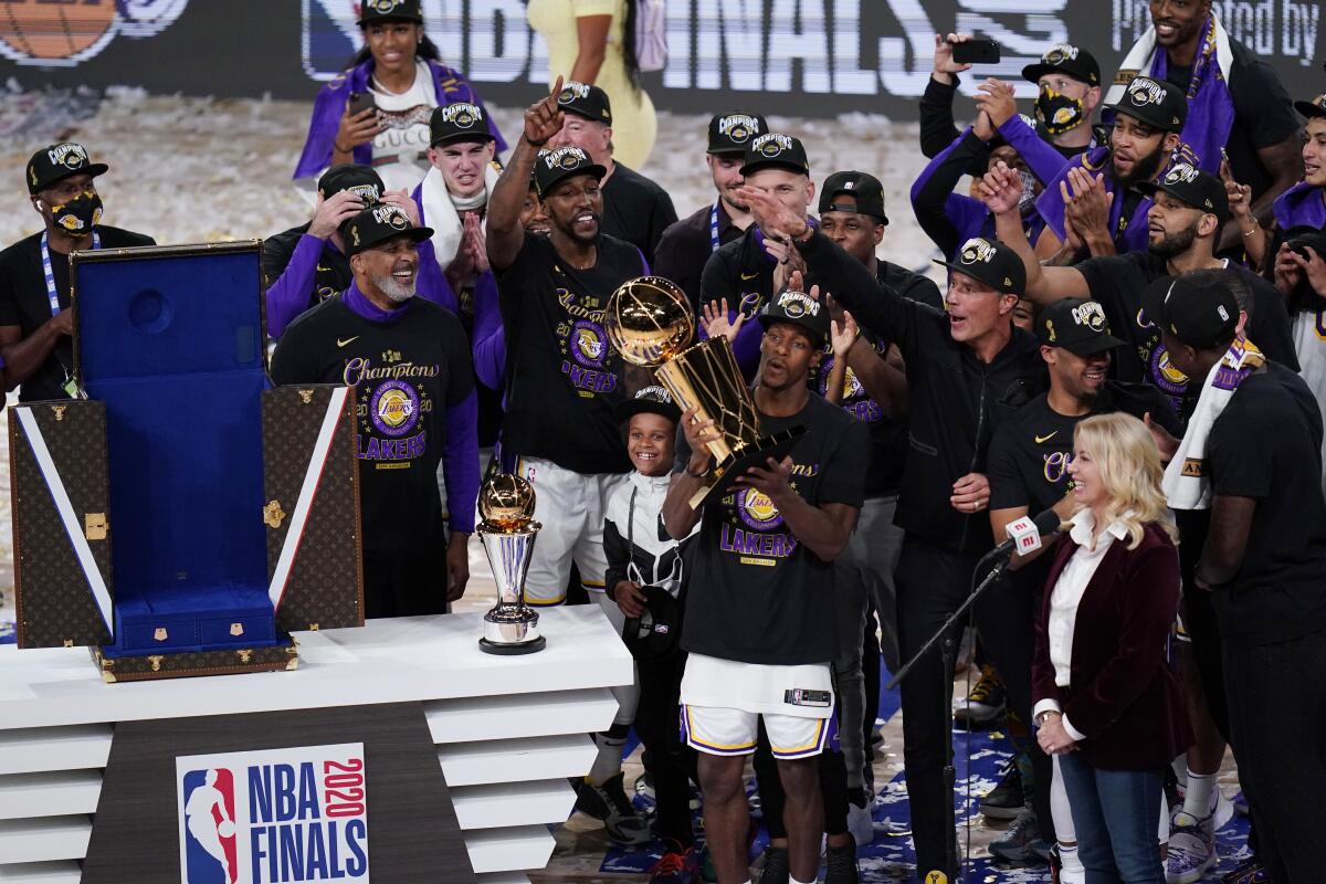 Lakers guard Rajon Rondo holds the championship trophy surrounded by teammates, coaches and executives Sunday night.