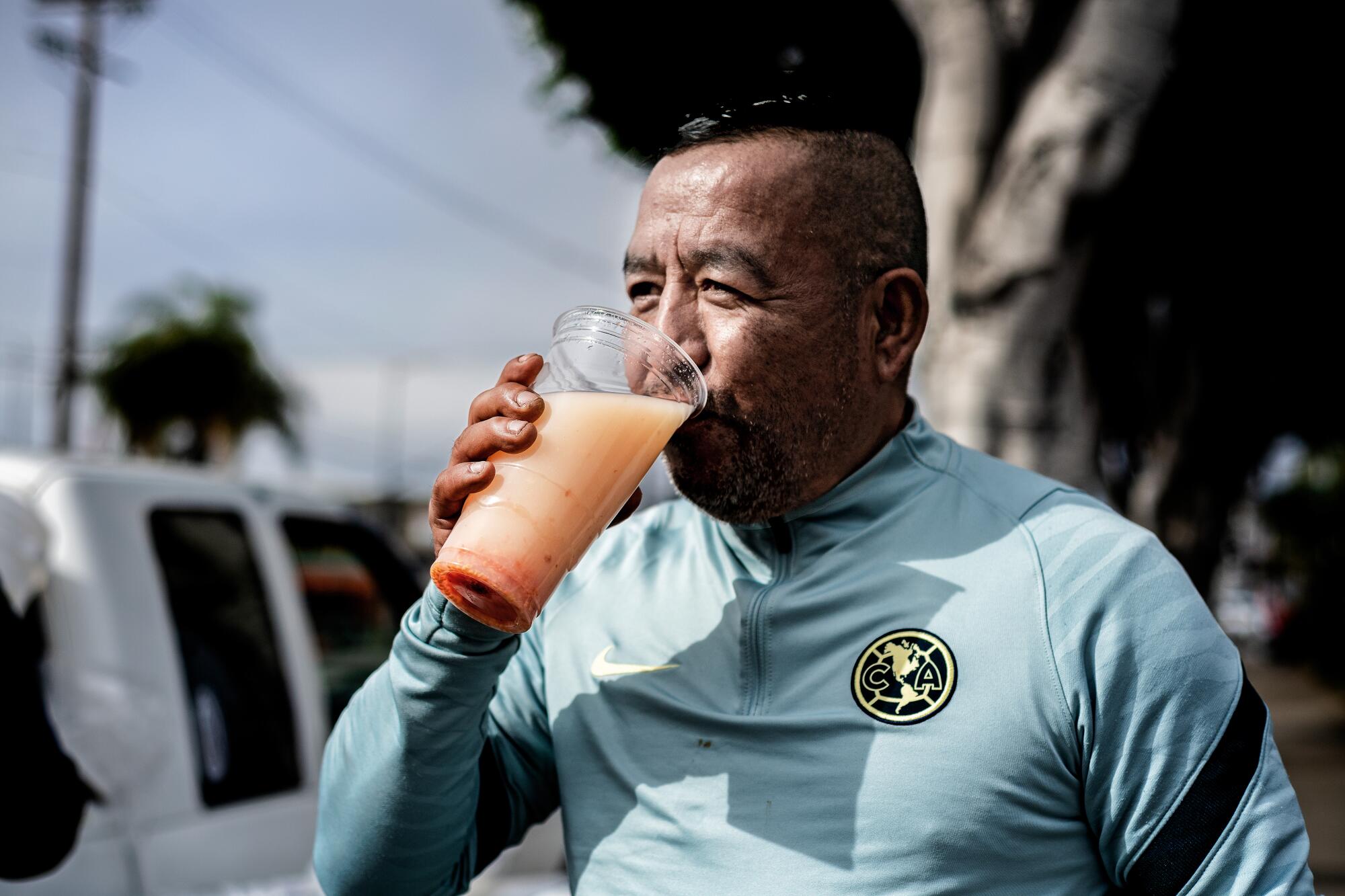 A man drinking from a large plastic cup full of pulque.