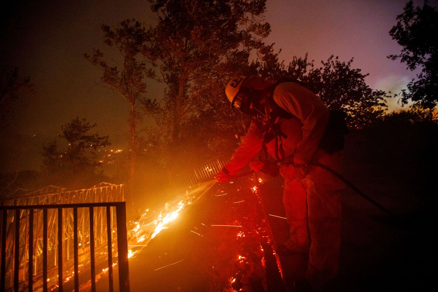 A firefighter uses a garden hose to douse flames in the backyard of a home to keep the Saddleridge fire from spreading in Porter Ranch.