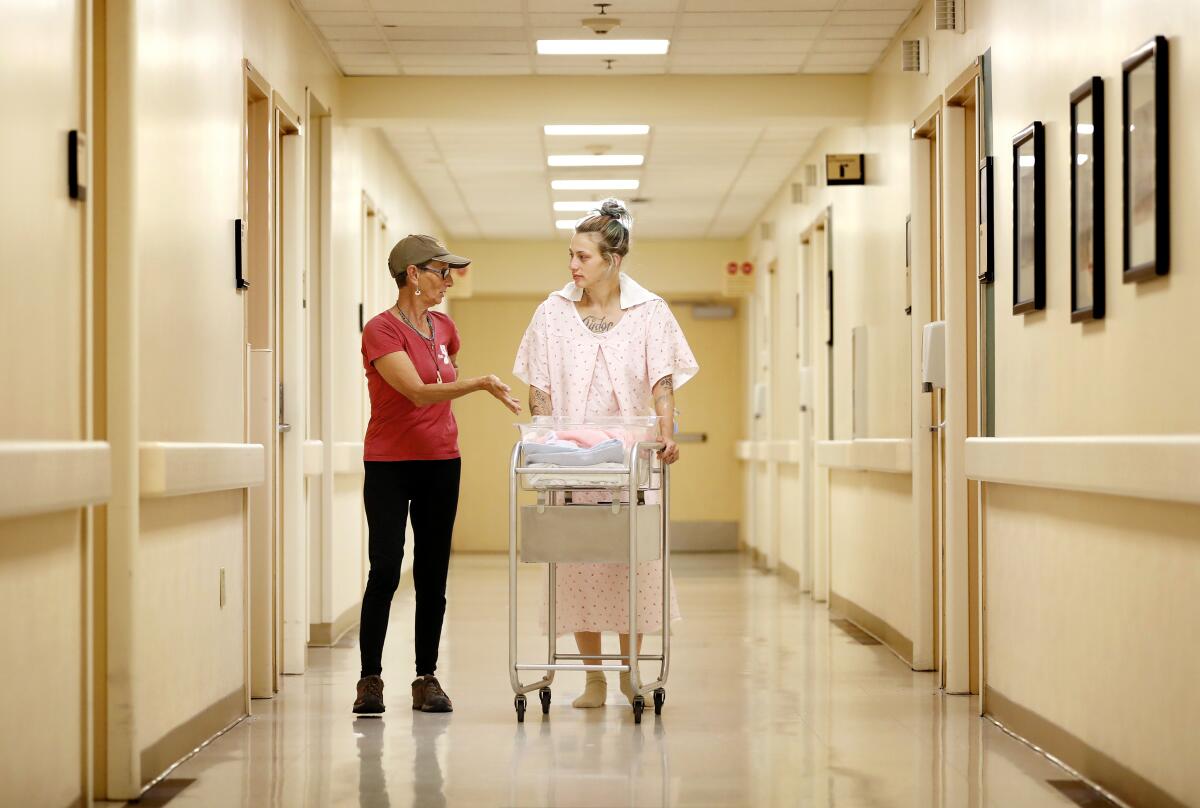 Two women walk in a hallway with a baby carrier