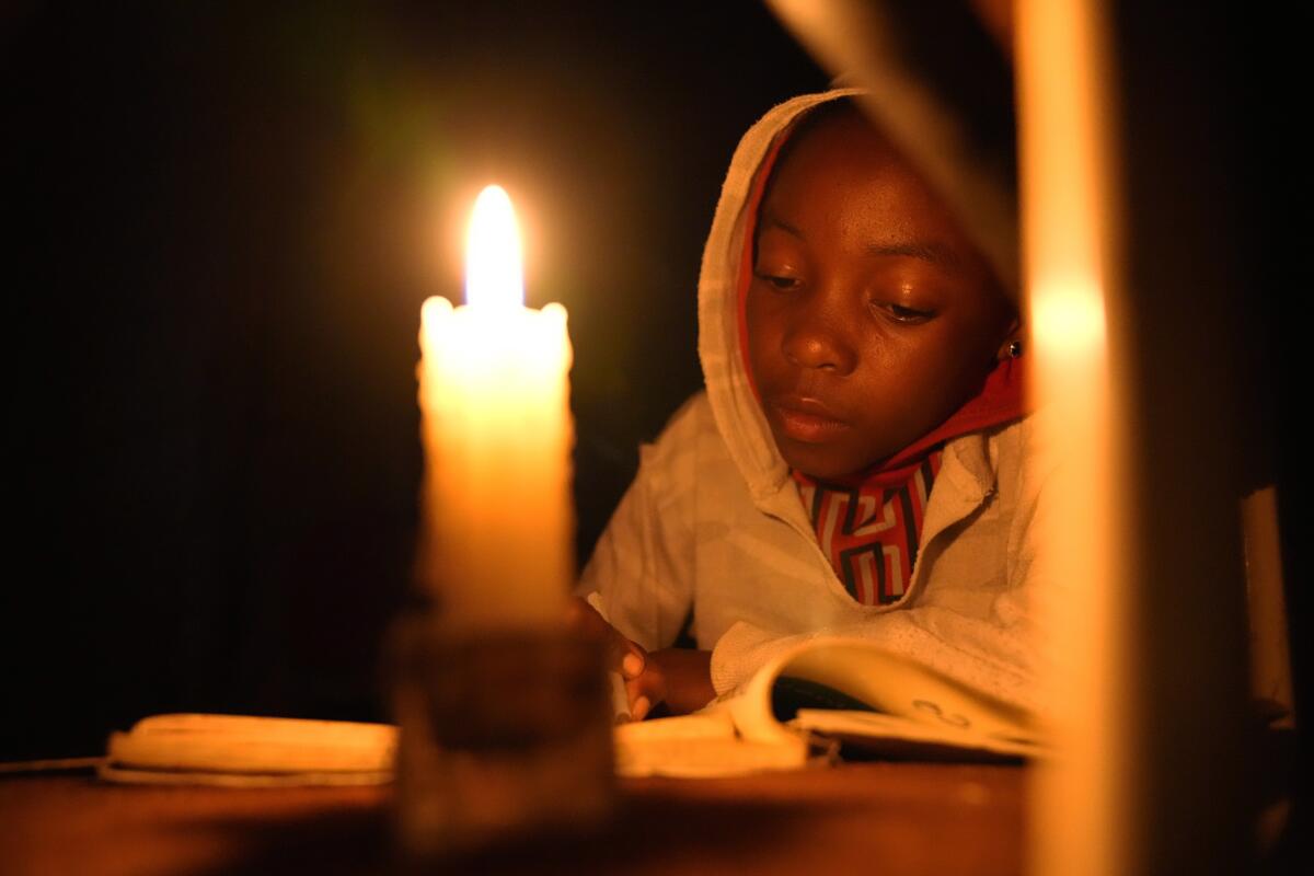 Tracy Carlos uses a candlelight to do her homework in Mabvuku on the outskirts of Harare on Wednesday, Aug, 3, 2022.Because of lengthy power cuts, the children do their homework by a candle, although their parents press them to use it sparingly. Her father Jeff Carlos says he gets about $100 dollars a month from his job as an overnight security guard for a church and the bar next door. Rising prices and a fast-depreciating currency have pushed many Zimbabweans to the brink, reminding people of when the southern African country faced world-record inflation of 5 billion % in 2008.(AP Photo/Tsvangirayi Mukwazhi)