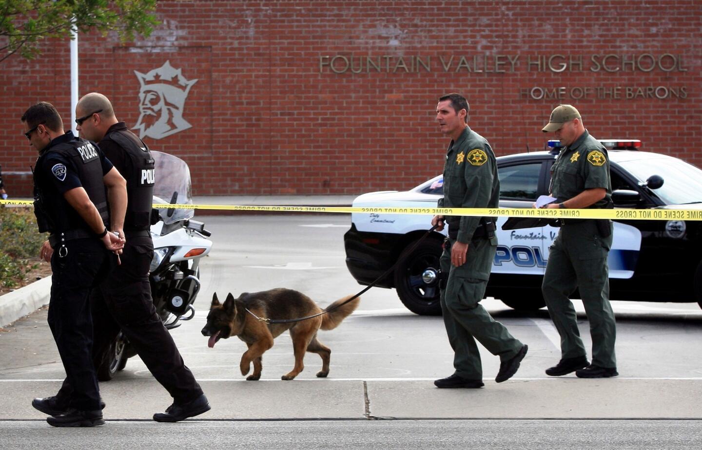 An Orange County sheriff's bomb-sniffing dog and Fountain Valley police investigate the scene at Fountain Valley High School. A threat of a bombing and mass shooting prompted officials to cancel classes.