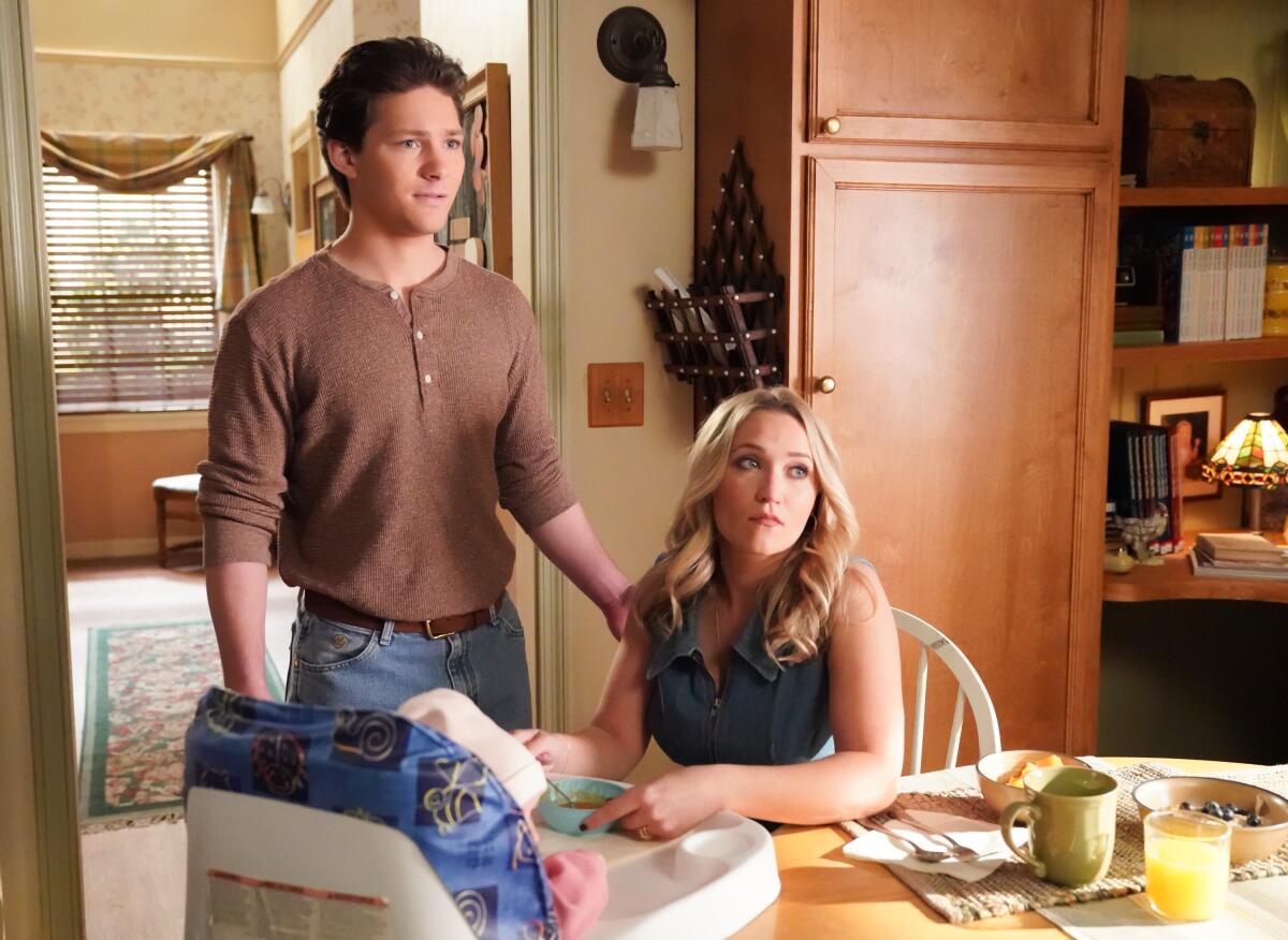 A man stands with a his hand on the shoulder of a woman sitting at a table.