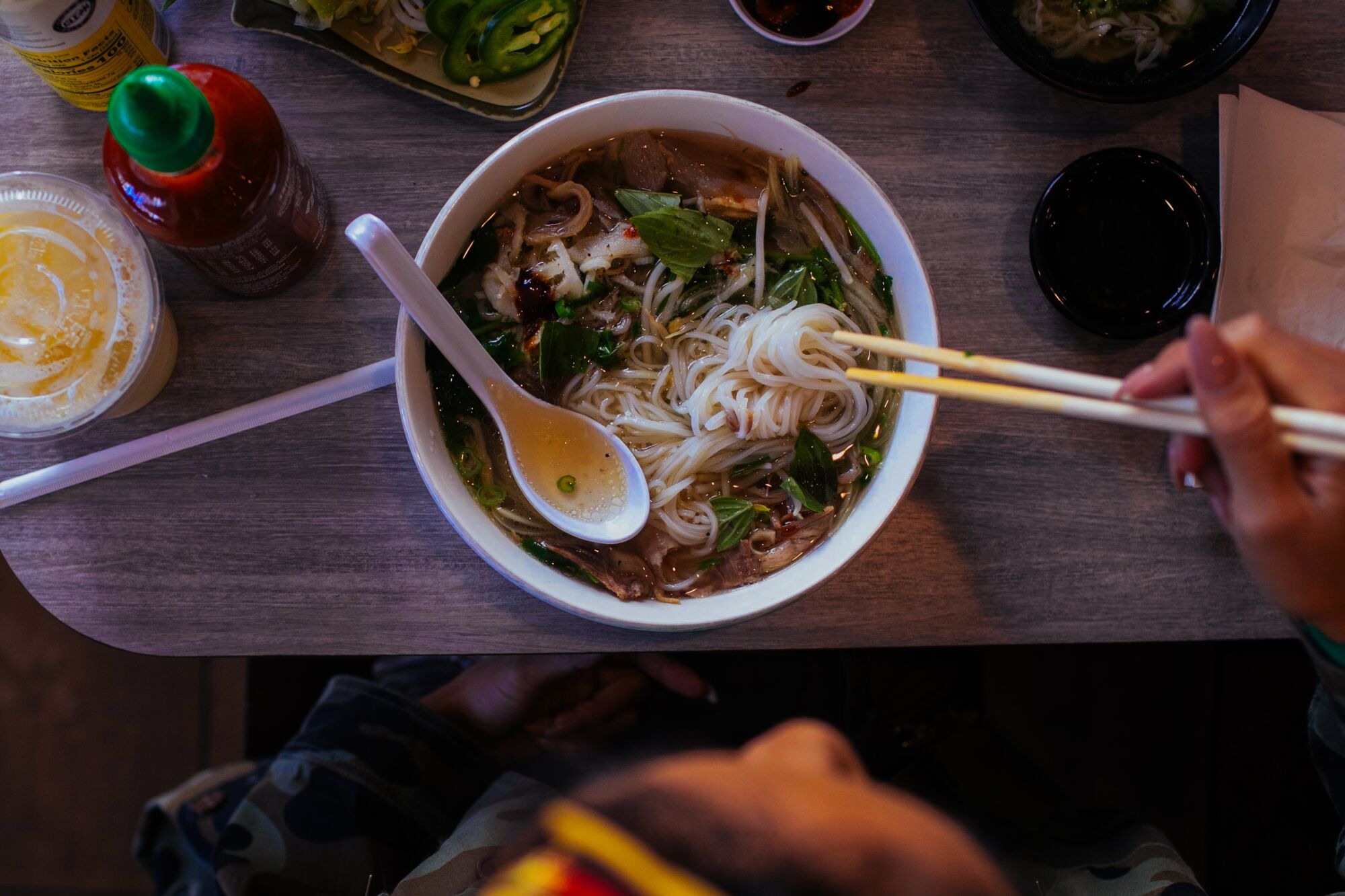 A person uses chopsticks to eat from a bowl of pho.