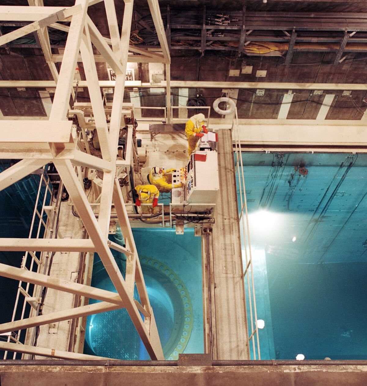 Water fills a reactor cavity as workers in yellow protective suits stand on a platform above it