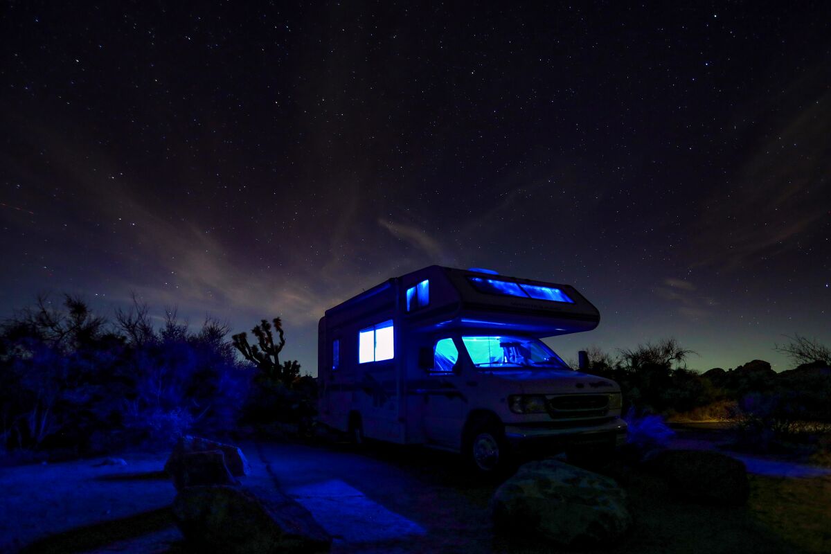 A lit-up RV camper and night sky in Joshua Tree National Park.
