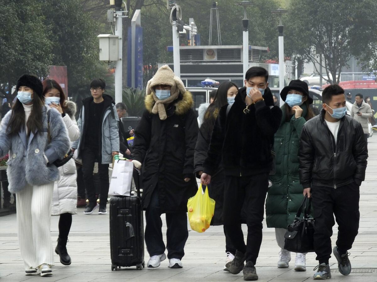 Viajeros usan mascarillas mientras caminan afuera de una estación de tren en Yichang, en la provincia de Hubei, en el sur de China, el martes 21 de enero de 2020. (Chinatopix via AP)