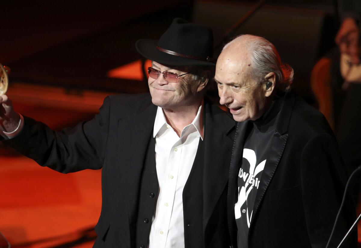 Two older men appear together onstage at a concert