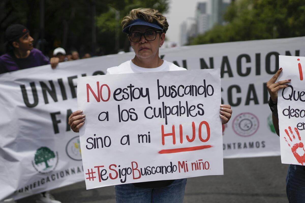 A woman holds a sign that reads in Spanish, "I'm not looking for those to blame, but for my son."