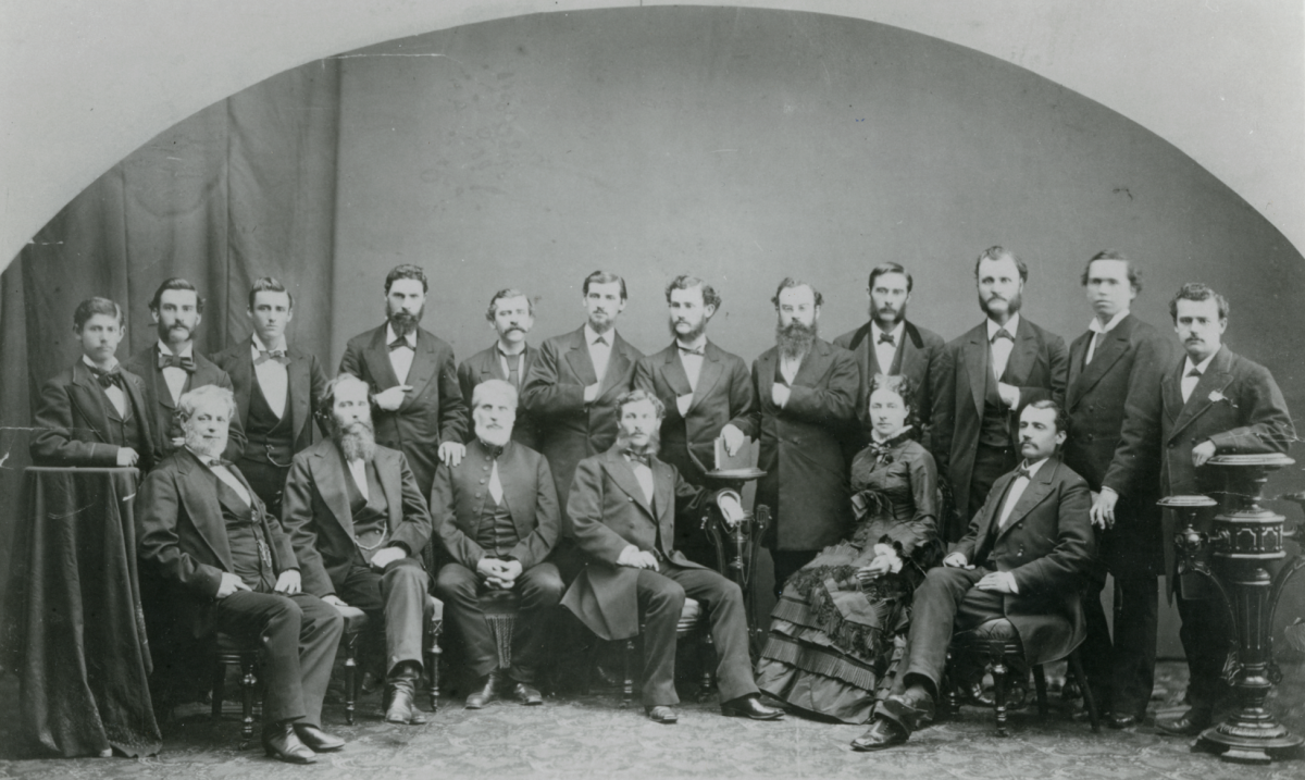 A group of 17 men and one woman pose for a formal photo.