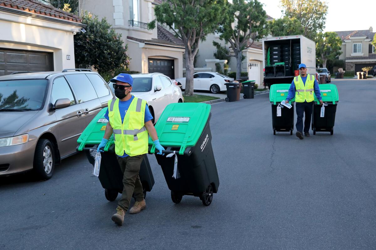 CR&R Environmental Services employees, Ceasar Garcia, left, and Jairo Acosta deliver new green-lid carts.