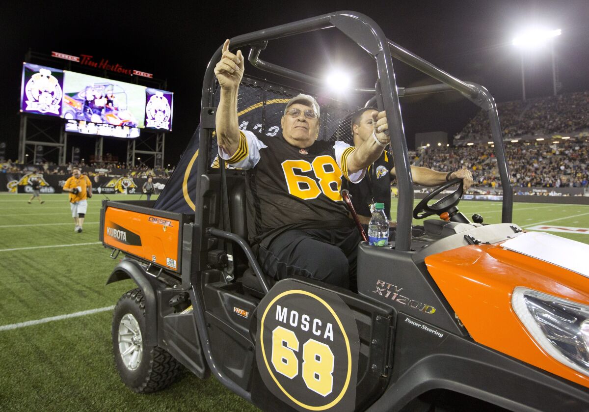 FILE - Hamilton Tiger-Cats alumnus Angelo Mosca is driven out onto the field in Hamilton, Ontario, Thursday, Aug. 27, 2015. Mosca, the five-time Grey Cup champion defensive lineman best remembered for a controversial hit and a subsequent fight with Joe Kapp 40 years later, died Saturday, Nov. 6, 2021. He was 84. (Peter Power/The Canadian Press via AP, File)