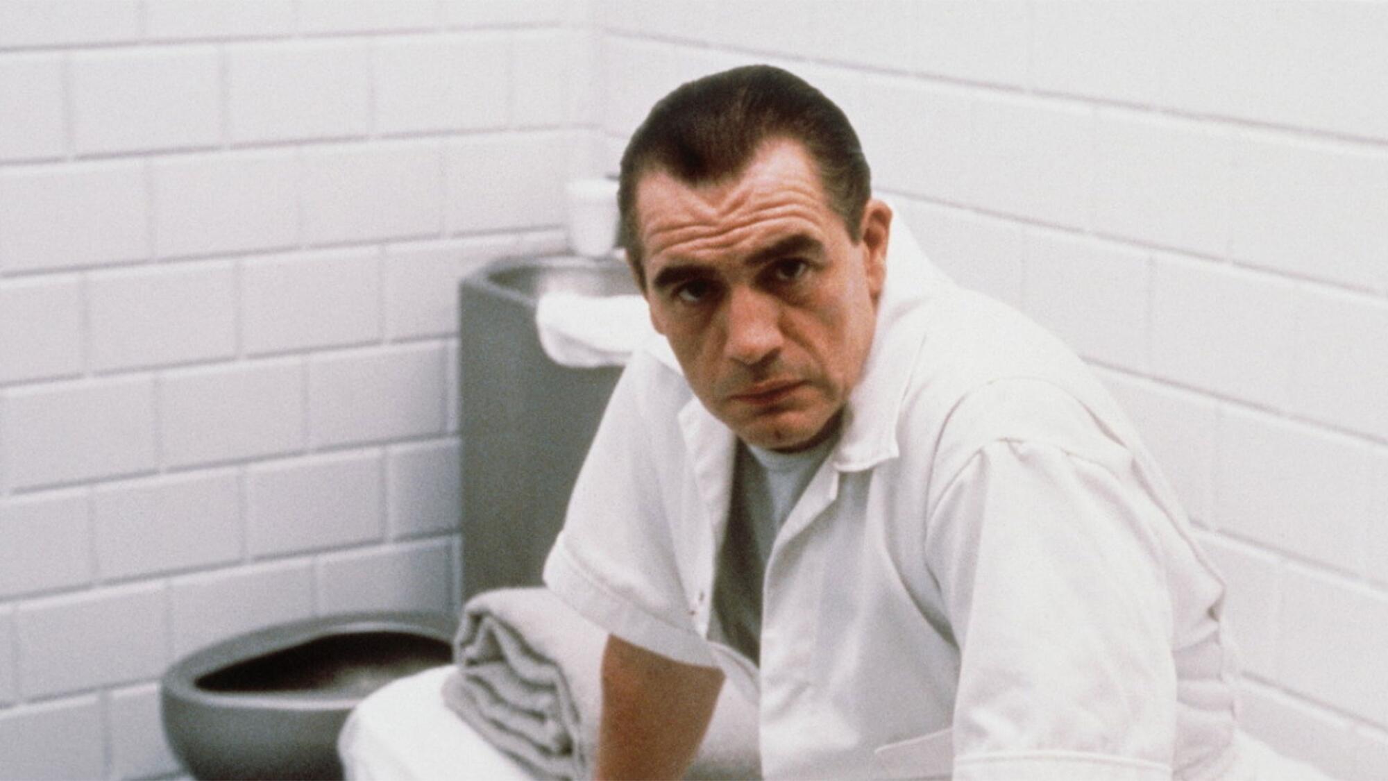 A man with a white coat is in a prison cell.