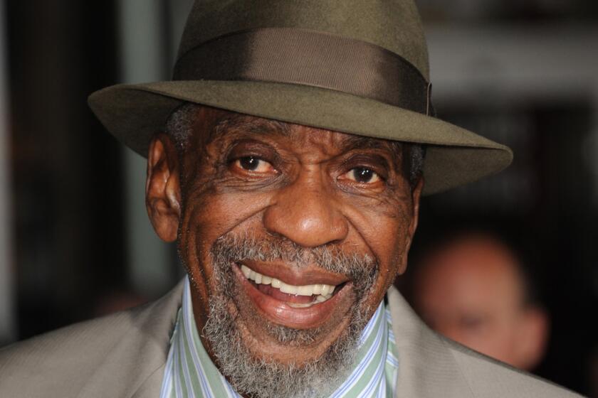 Bill Cobbs smiling broadly in a taupe suit and greenish-brown fedora