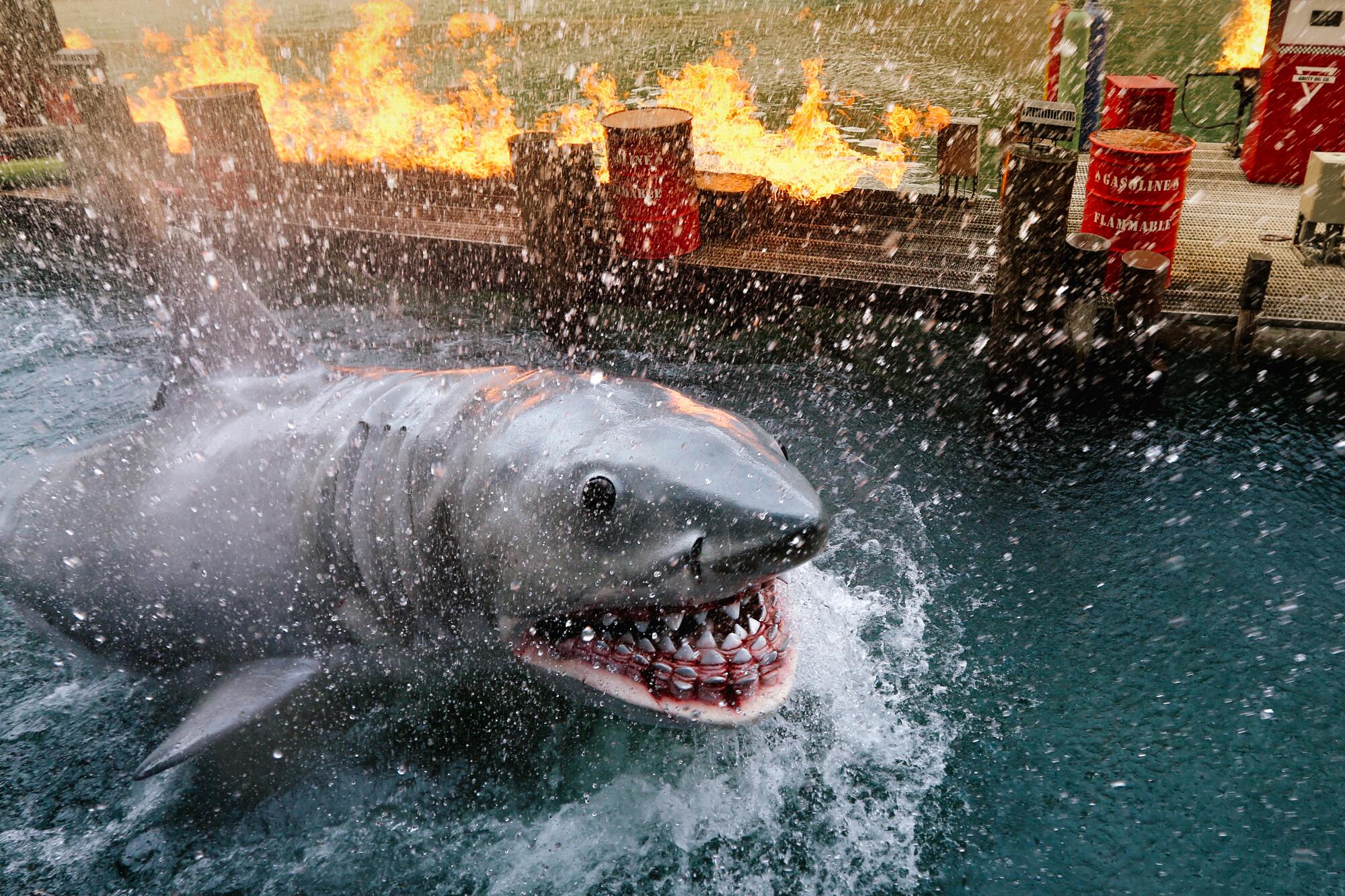 A shark churns the water alongside a burning dock.