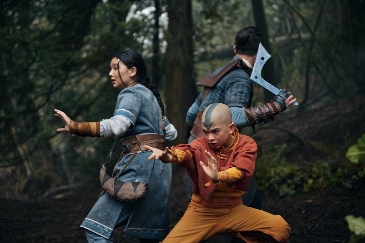 Three children gathered in fighting postures in the middle of a forest.