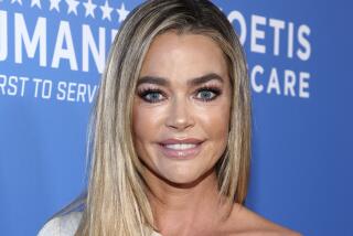 Denise Richards poses in a white dress at an event. 
