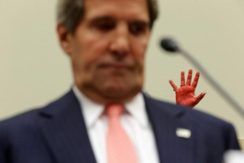 A protester holds up her hand, covered in red paint symbolizing blood, as Secretary of State John F. Kerry testifies Wednesday during a House hearing on proposed military strikes against Syria.