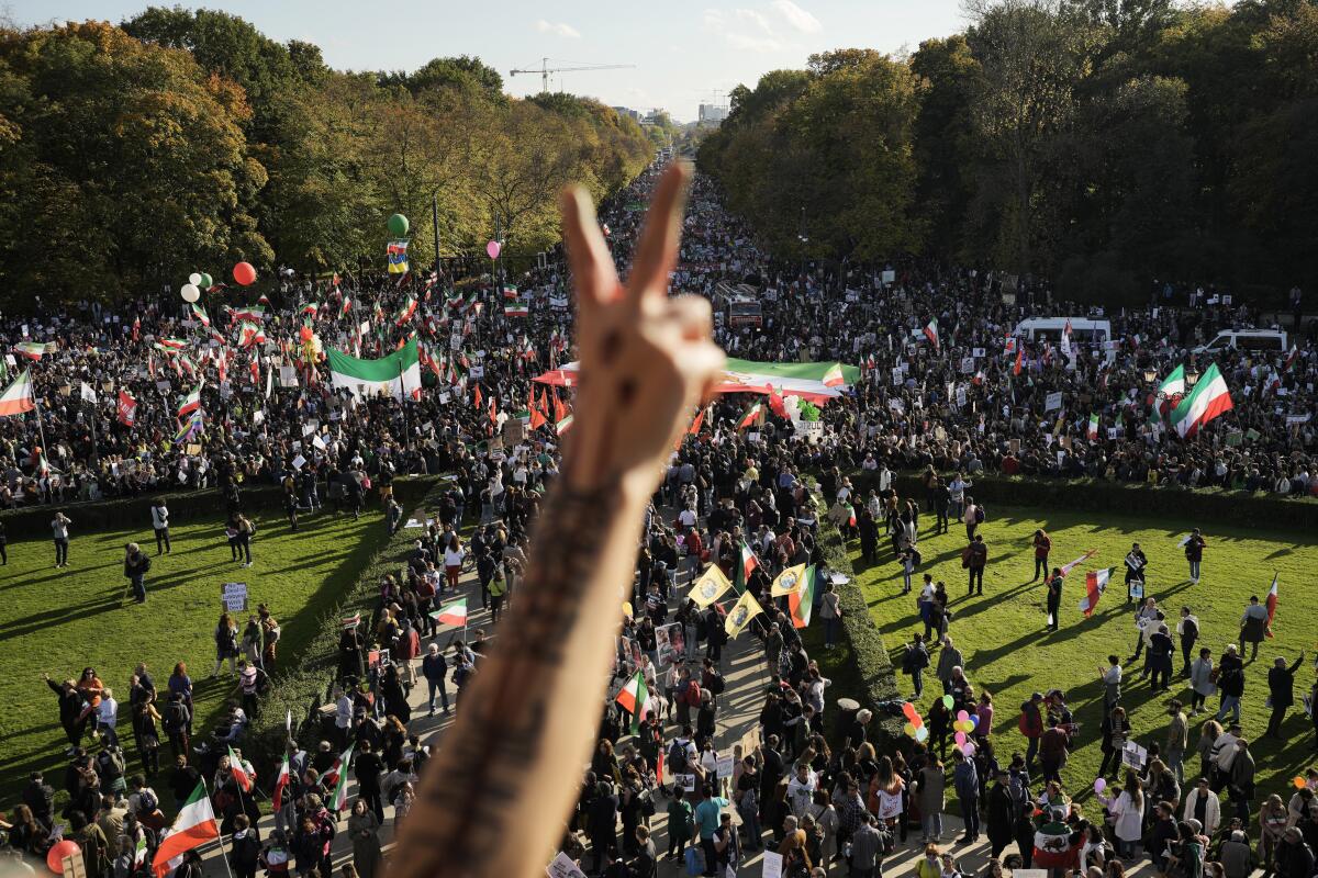 A hand with two fingers raised before a large crowd of demonstrators on a field. 