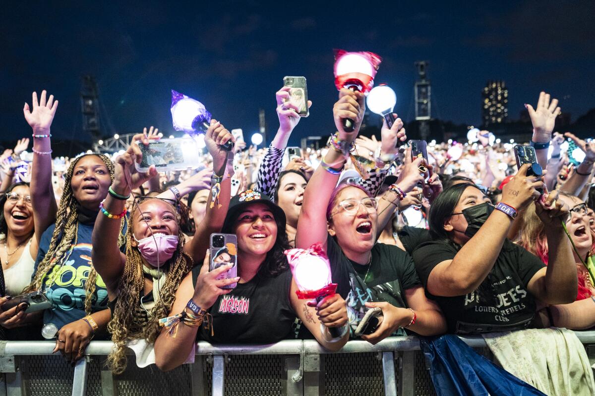 A crowd of smiling, cheering concertgoers in stadium seating reach out their hands and film with their phones.
