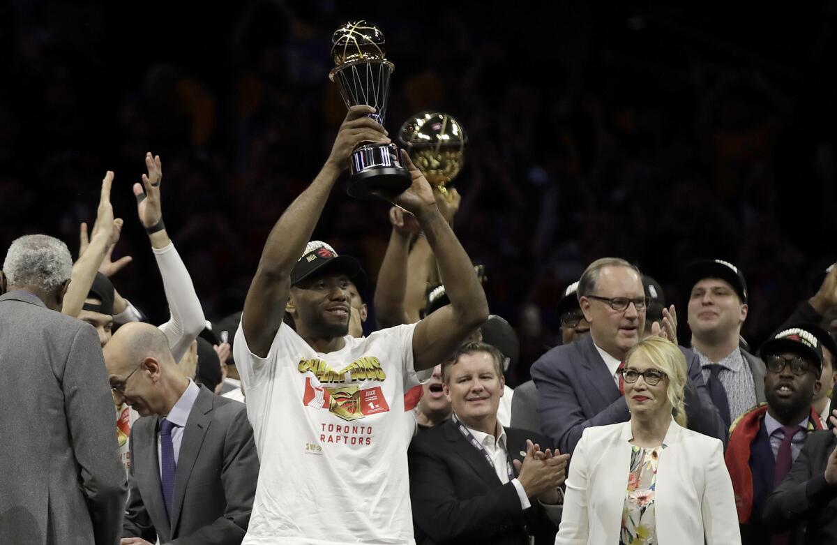 Kawhi Leonard last June hoisting his second NBA Finals MVP trophy, surrounded by a crowd.