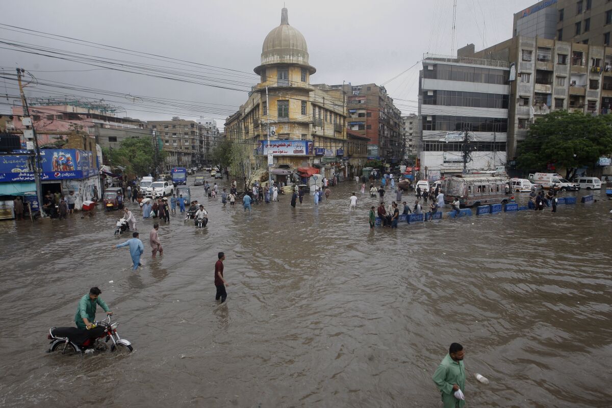 Motorcyclists and people wade through a flooded road in a business district after a heavy rainfall in Karachi, Pakistan, Saturday, July 9, 2022. Several people have died in rain-related incidents across Pakistan during the past three weeks, a top officials said. (AP Photo/Fareed Khan)