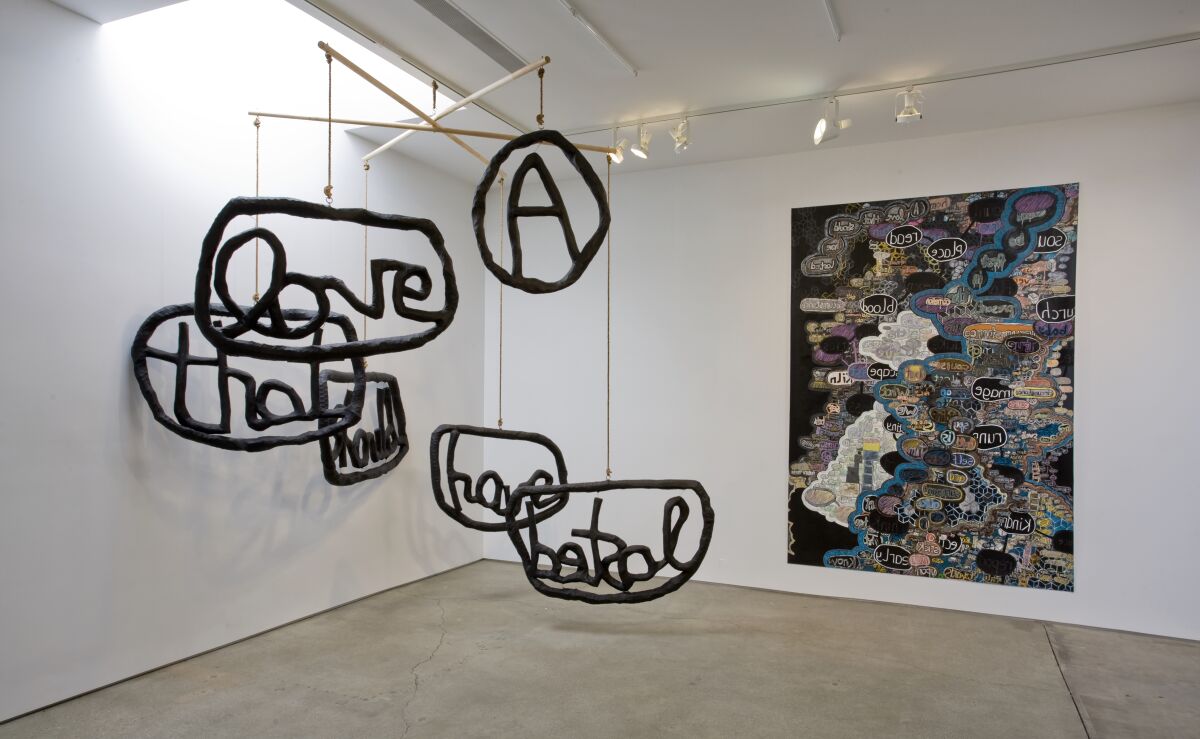Mobile with sculptures of words hanging from it, left, and a painting on the wall