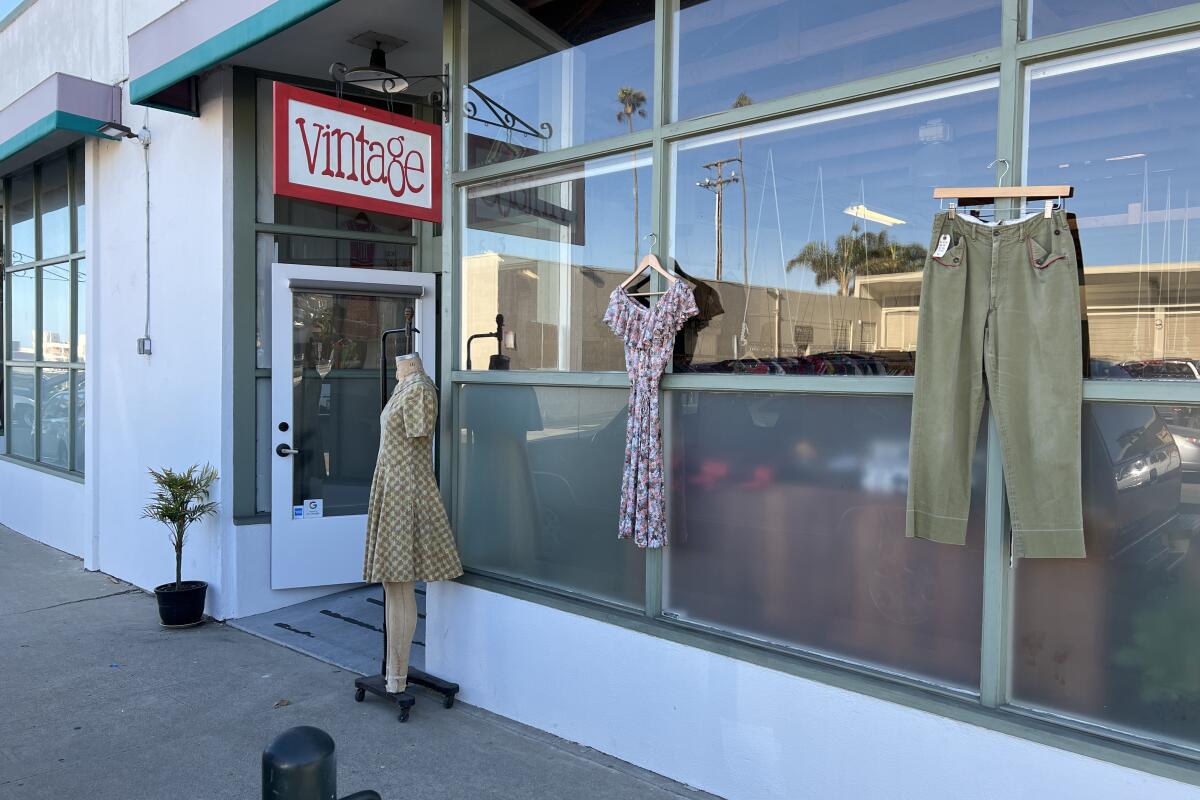 Two dresses and a pair of pants on display outside a store with a sign that says "Vintage"