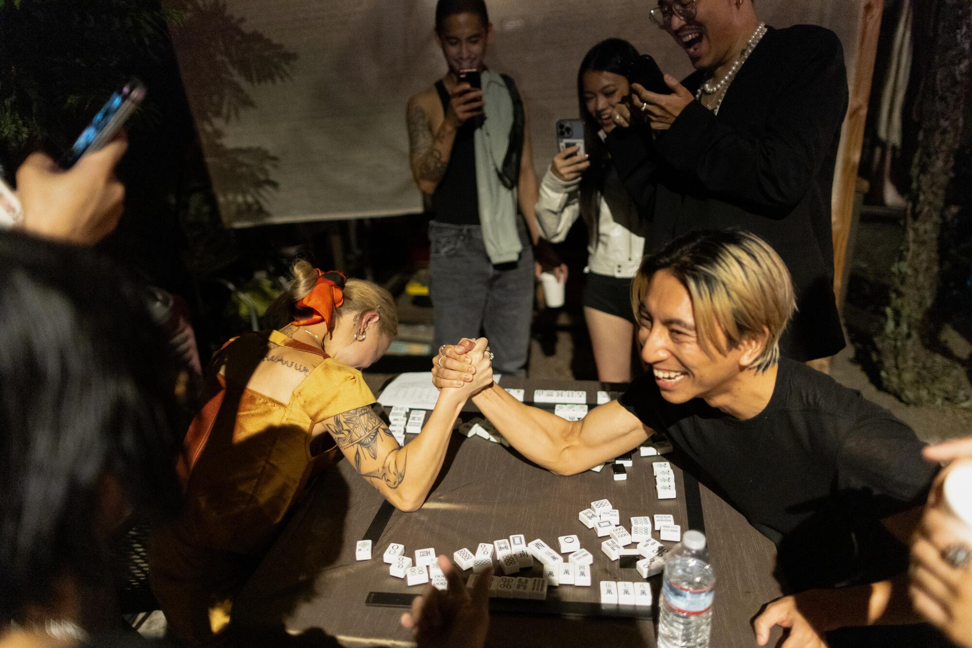 Two people arm-wrestle amid mah-jongg tiles. 