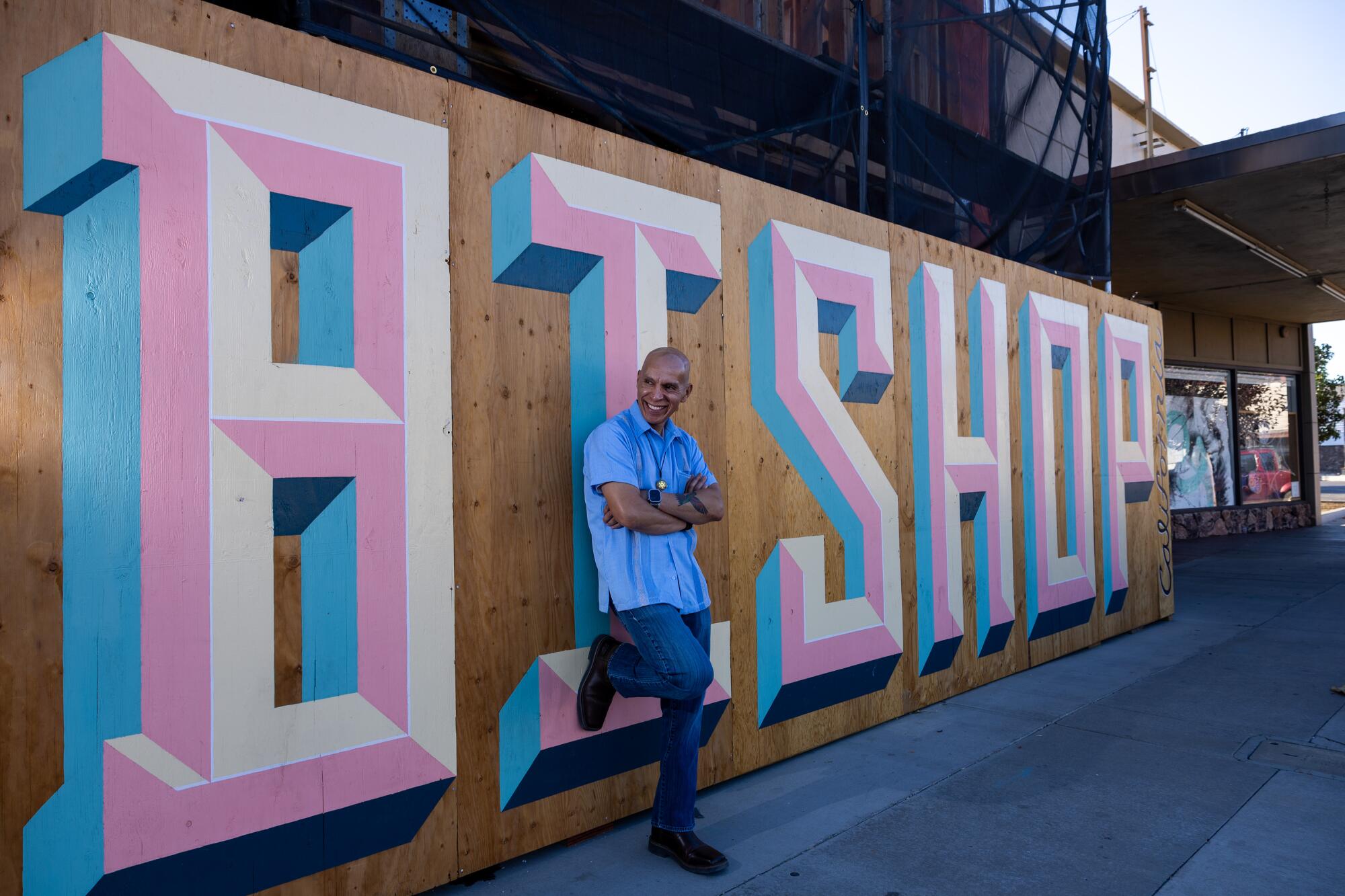 A man stands next to a mural that spells the name "Bishop." 