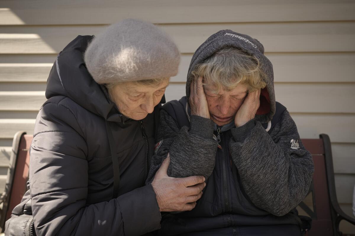 A woman comforts her neighbor whose husband and grandson were killed by Russian forces.
