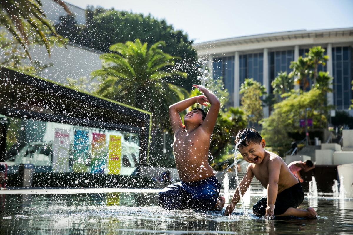 Nathan Gomez, 2, right, learns to mimic his older brother, Matthew Gomez, 9, left, as they use their heads to fling water in the air while playing at the water fountain at Grand Park.