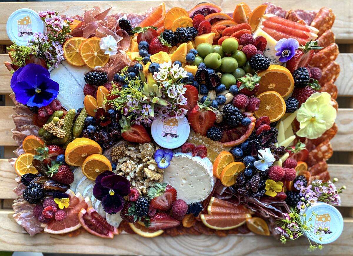 A board full of fruits, flowers, meats, nuts and cheeses