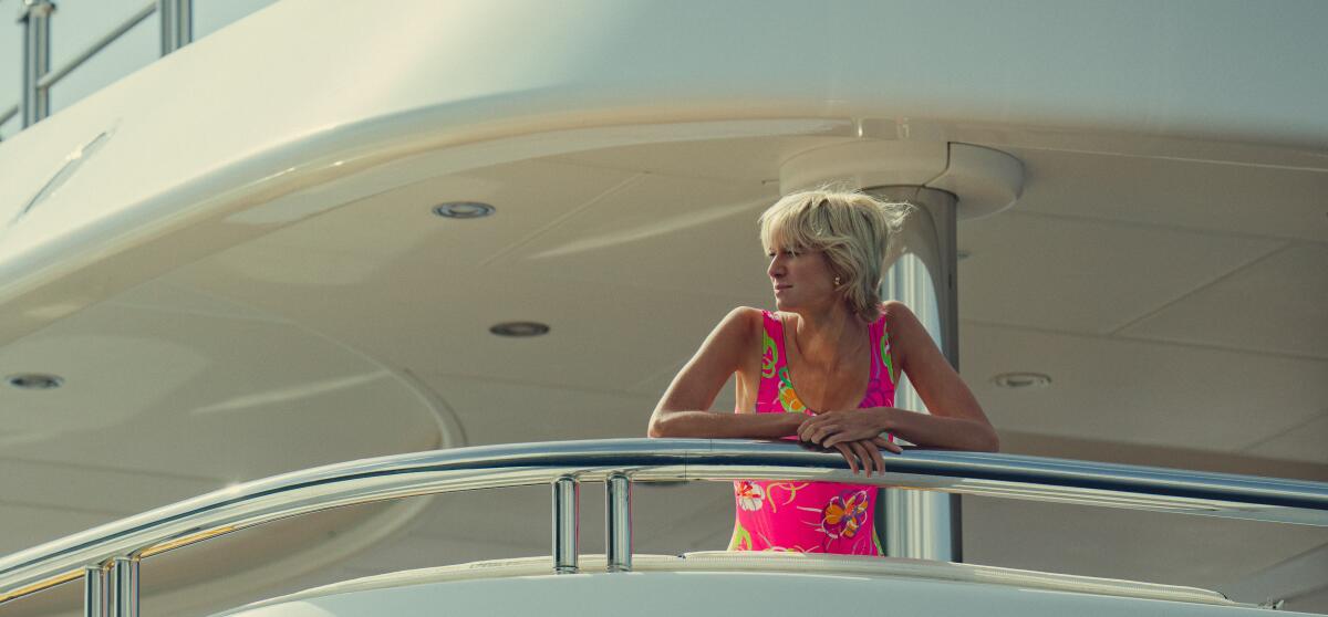 A woman with short blond hair wears a swimsuit as she stands at the railing of a yacht in "The Crown."