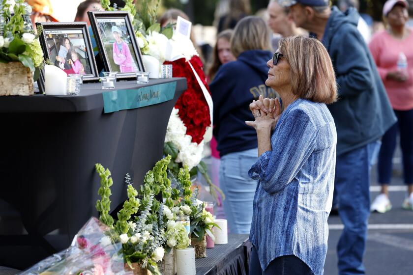 A woman stands before a photo of Raleigh shooting victim Susan Karnatz at a makeshift memorial at the Hedingham neighborhood. (Ethan Hyman/The News & Observer via AP)