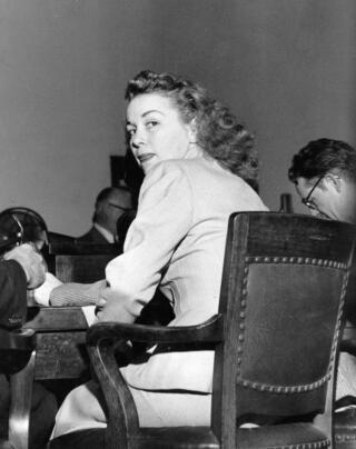 Barbara Graham looks over her shoulder while seated at a courtroom table.