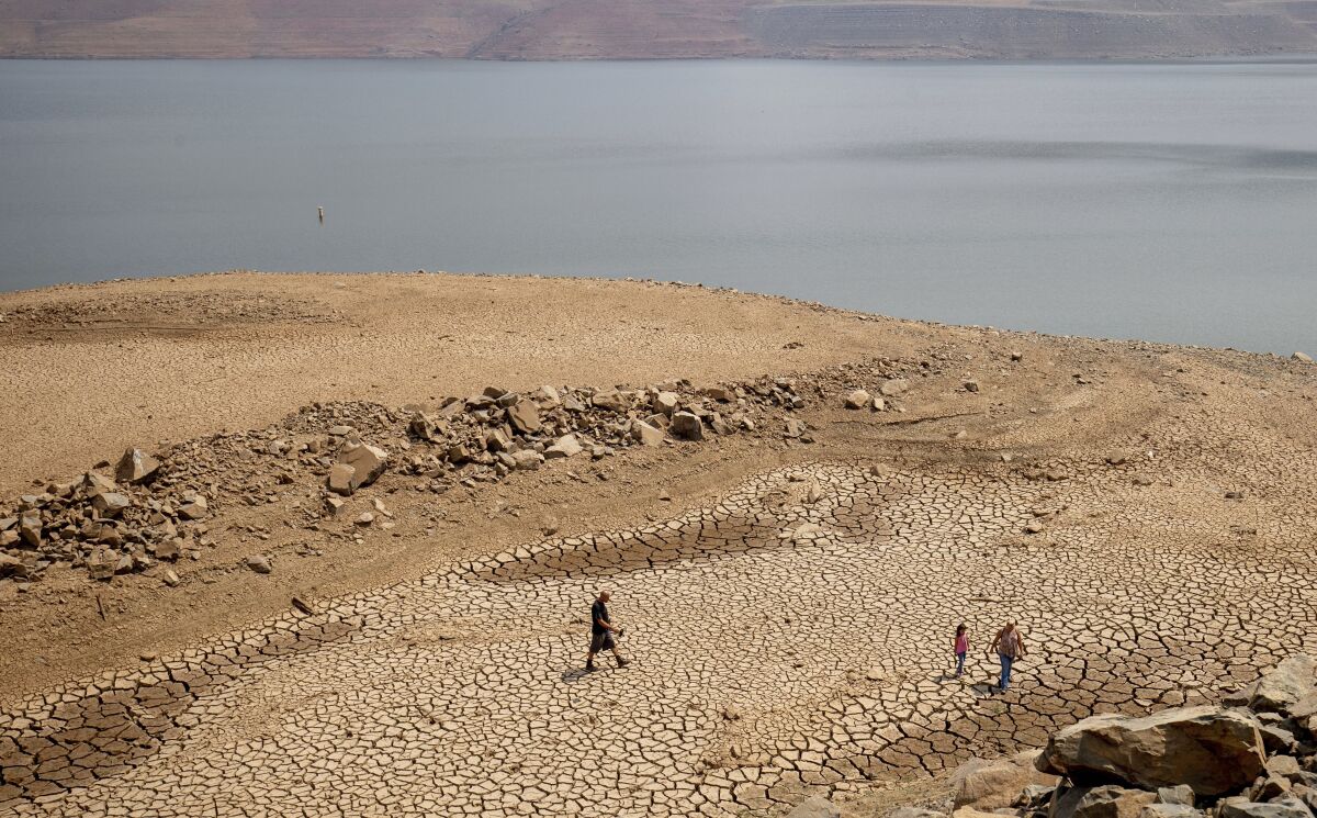 FILE — In this Aug. 22, 2021, file photo, a family walks over cracked mud near Lake Oroville's shore