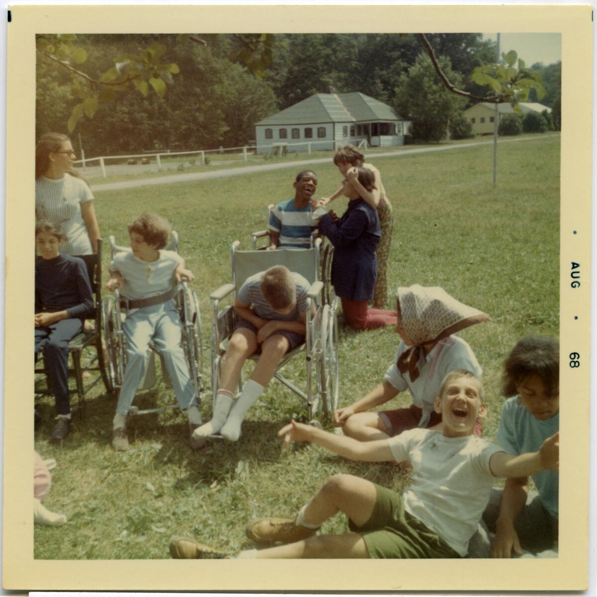 Several children using wheelchairs and others are seen in the sunshine on a grassy field in a 1968 photo.