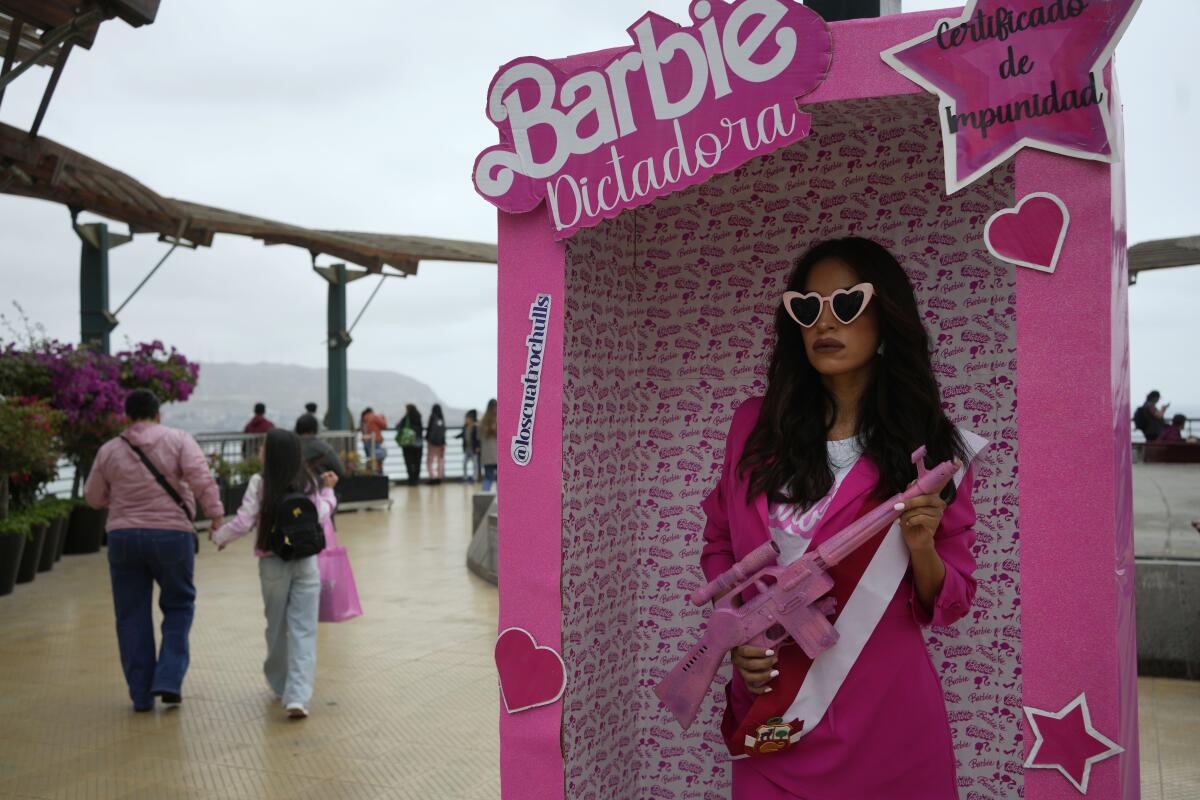 A woman holding a pink gun stands in a giant pink box reading "Dictator Barbie" in Spanish.