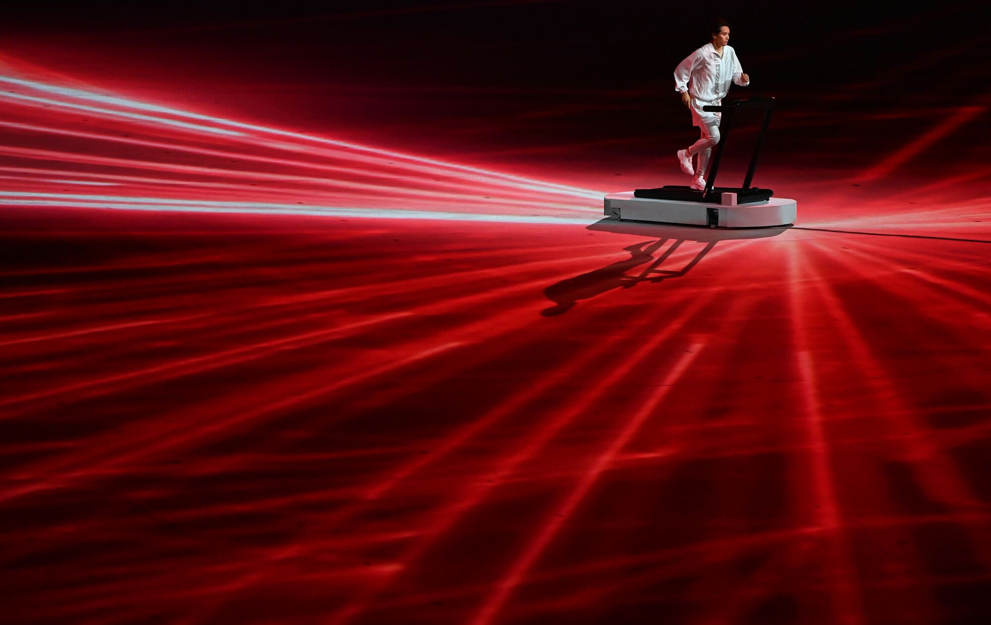 A man runs on a treadmill onstage surrounded by laser lights