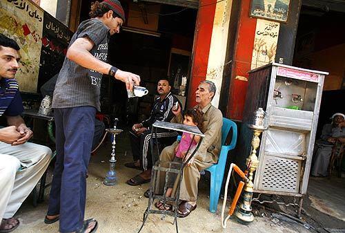 Mosad Shawki holds his granddaughter while ordering tea at a shop in Cairo, where he and his nephew Ramzi, next to him, are garbage collectors who raised pigs.