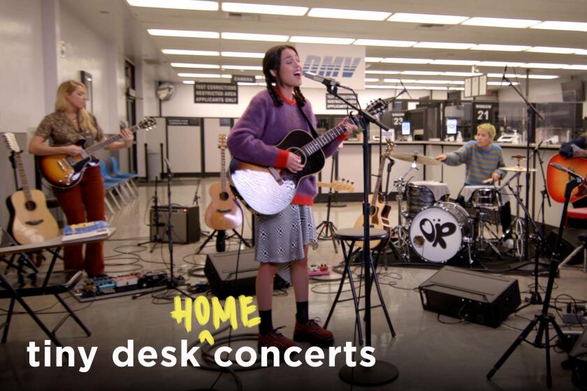 A woman playing guitar and singing into a microphone in front of a band at a DMV