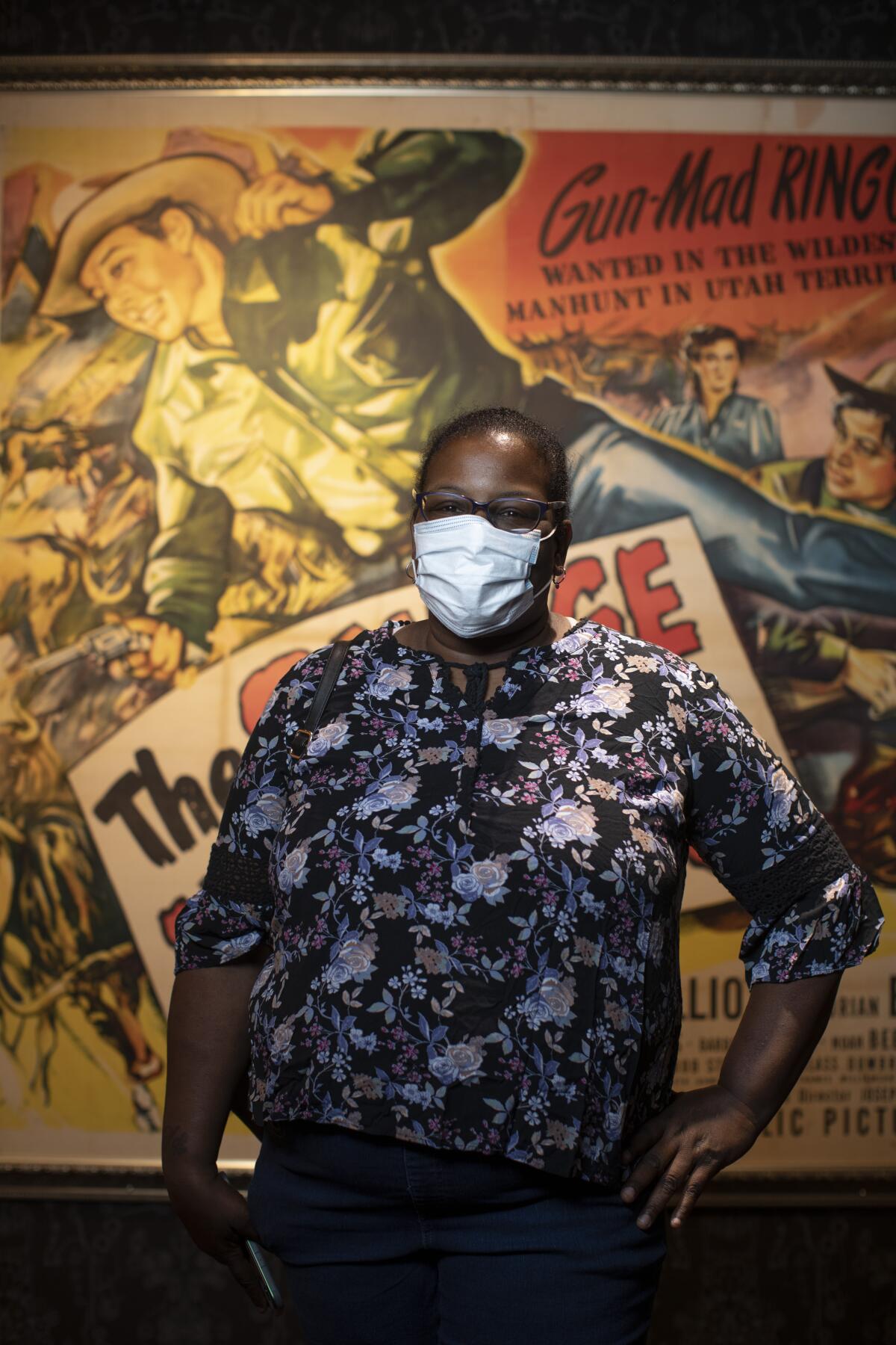 Brenda Williams wearing a mask stands in front of a movie poster.