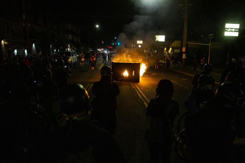 A waste receptacle is set on fire near the Portland Police Association building during a protest in Portland, Ore., on Tuesday, Aug. 4, 2020. A riot was declared early Wednesday during demonstrations in Portland after authorities said people set fires and barricaded public roadways.(Dave Killen /The Oregonian via AP)