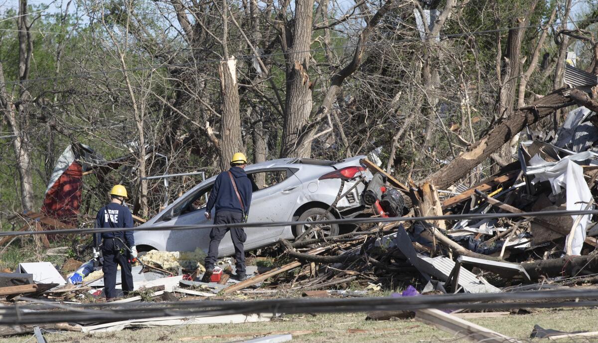 Firefighters inspect a wrecked car atop downed trees and other debris