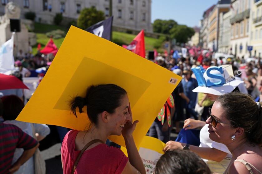 A protestor shades herself from the sun behind her poster in hot weather during a demonstration by workers' unions outside the parliament in Lisbon, Thursday, July 7, 2022. Portugal is bracing for a heat wave, with temperatures in some areas forecast to climb as high as 43 degrees Celsius, 109 degrees Fahrenheit, this weekend. The high temperatures are expected to last at least a week. (AP Photo/Armando Franca)