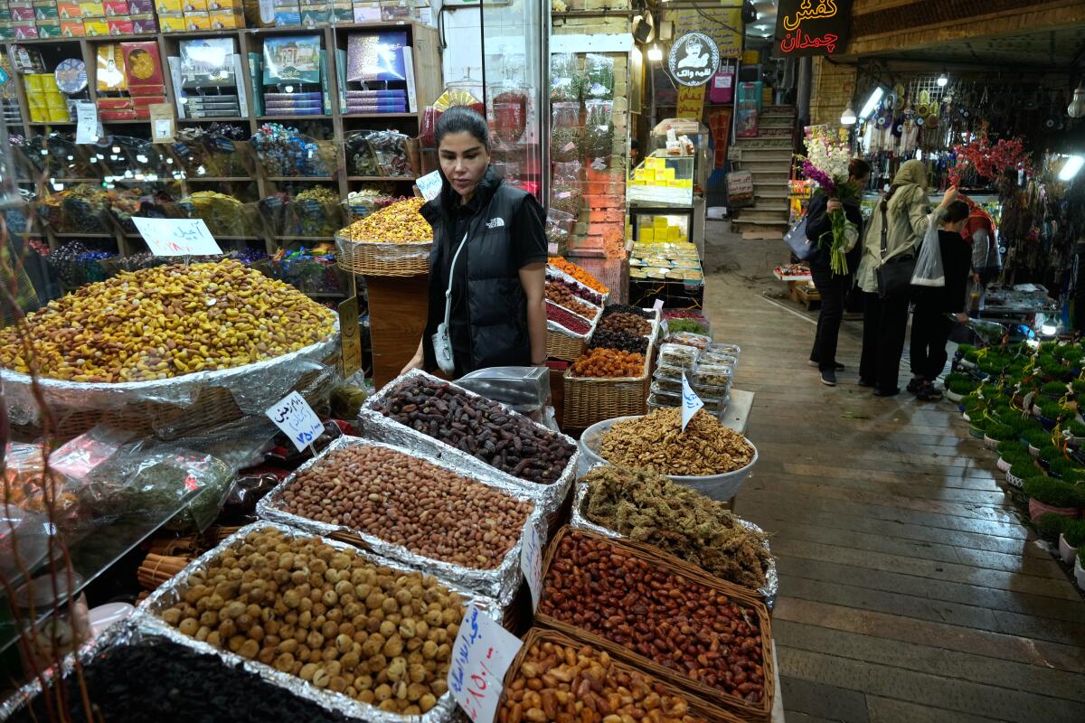 A woman with dark hair, in dark clothes, stands looking at a trays of snacks at an indoor stall