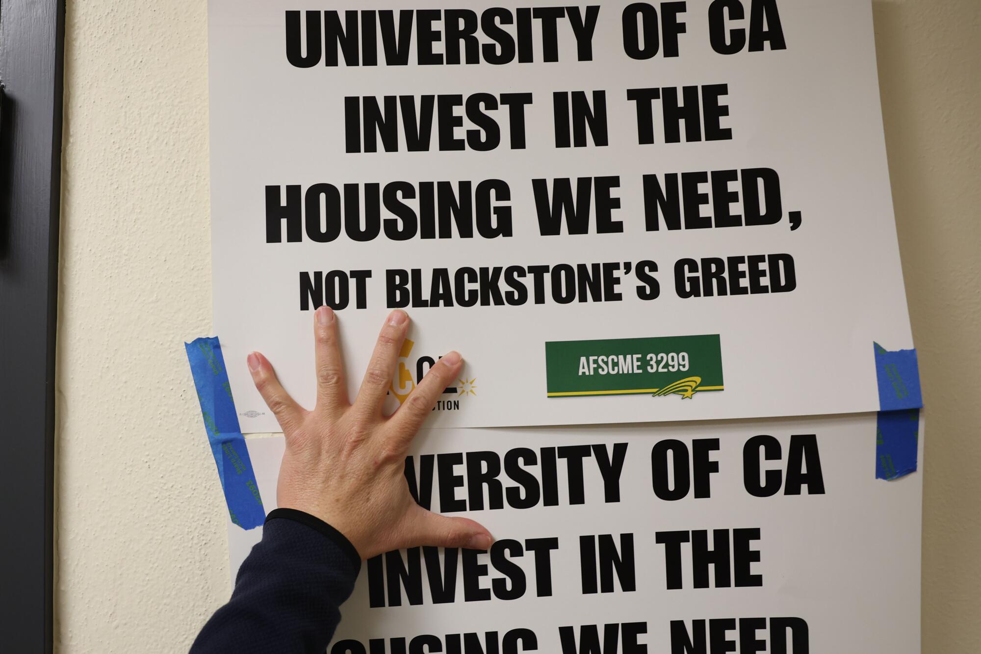 Signs reading "University of CA invest in the housing we need, not Blackstone's greed" are taped to a wall.